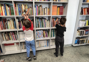 Dzieci stoją przy regale i oglądają książki w bibliotece szkolnej.