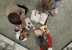 Dzieci siedzą i oglądają książki w bibliotece szkolnej.