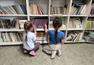 Dzieci przy regale i oglądają książki w bibliotece szkolnej.