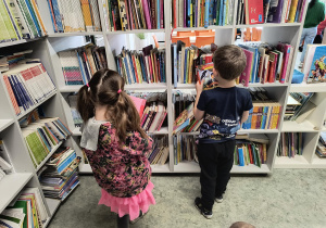 Dzieci stoją przy regale i oglądają książki w bibliotece szkolnej.
