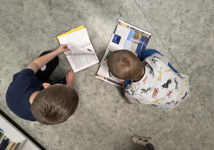 Dzieci siedzą i oglądają książki w bibliotece szkolnej.