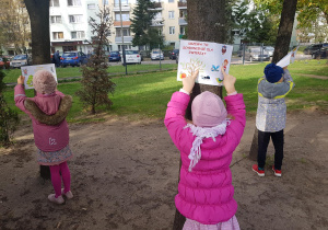 Dzieci instalują w ogrodzie plakaty ekologiczne.
