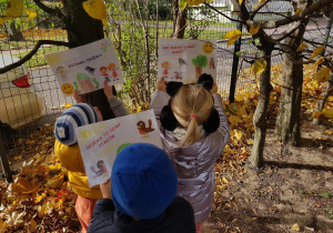 Dzieci instalują w ogrodzie plakaty ekologiczne.