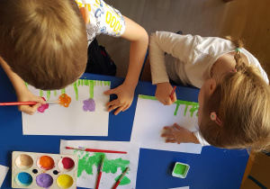 Dzieci malują farbami kolorowe kwiaty.