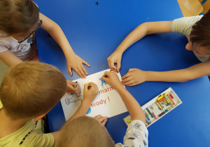 Dzieci przygotowują kolorowe ulotki na temat oszczędzania wody.