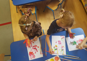 Dzieci pokrywają dłonie farbami plakatowymi. Odciskają swoje dłonie na kartonach.