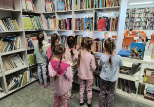 Dzieci stoją przy regale i oglądają książki w bibliotece szkolnej.