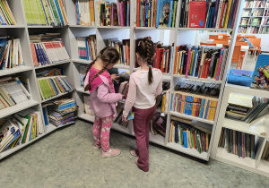 Dzieci stoją przy regale i oglądają książki w bibliotece szkolnej.