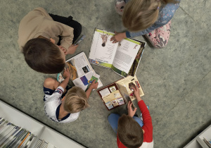 Dzieci siedzą i oglądają książki w bibliotece szkolnej.