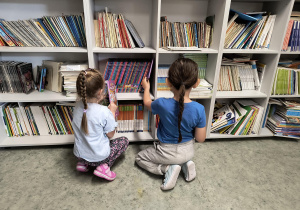 Dzieci przy regale i oglądają książki w bibliotece szkolnej.