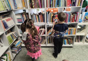 Dzieci stoją przy regale i oglądają książki w bibliotece szkolnej.