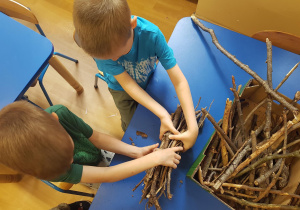 Dzieci ukłądają patyki i tworząc domki dla owadów.