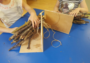 Dzieci umieszczają ułożone patyki pod daszkiem domku dla owadów