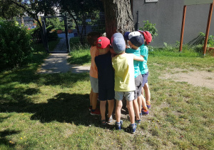 Dzieci przytulają się do drzewa w ogrodzie.