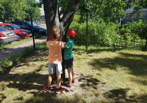Dzieci przytulają się do drzewa w ogrodzie.