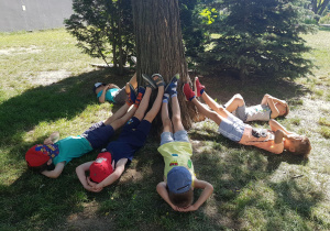Dzieci leżą dookoła drzewa opierając nogi o pień.