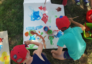 Dzieci malują farbami na dużych arkuszach.