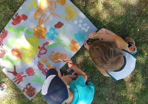 Dzieci malują farbami na dużych arkuszach.