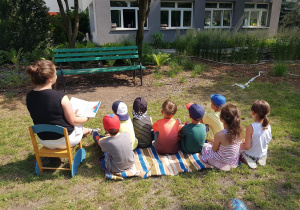 Dzieci siedzą na kocu w ogrodzie przedszkolnym.