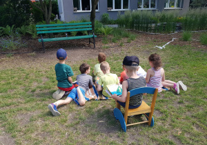Dzieci siedzą na kocu w ogrodzie przedszkolnym.