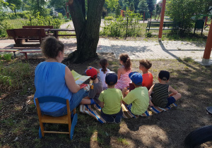 Dzieci siedzą na kocu w ogrodzie przedszkolnym.