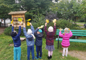 Grupa dzieci stoi w ogrodzie. Dzieci trzymają w rękach żółte liście.