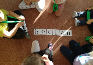 Dzieci siedzą na dywanie i układają napis bocian.