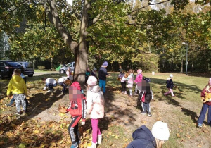 Grupa dzieci zbiera liście w parku.
