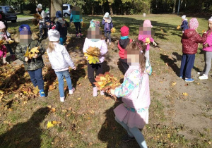 Grupa dzieci zbiera liście w parku.
